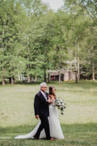 A bride walks down the aisle with her father on a farm in springtime.